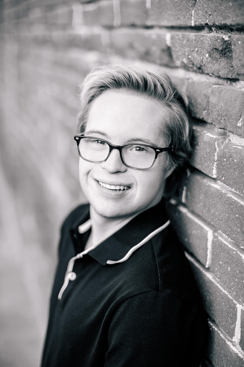 Professional black and white head shot of Cole smiling and leaning against a brick wall.