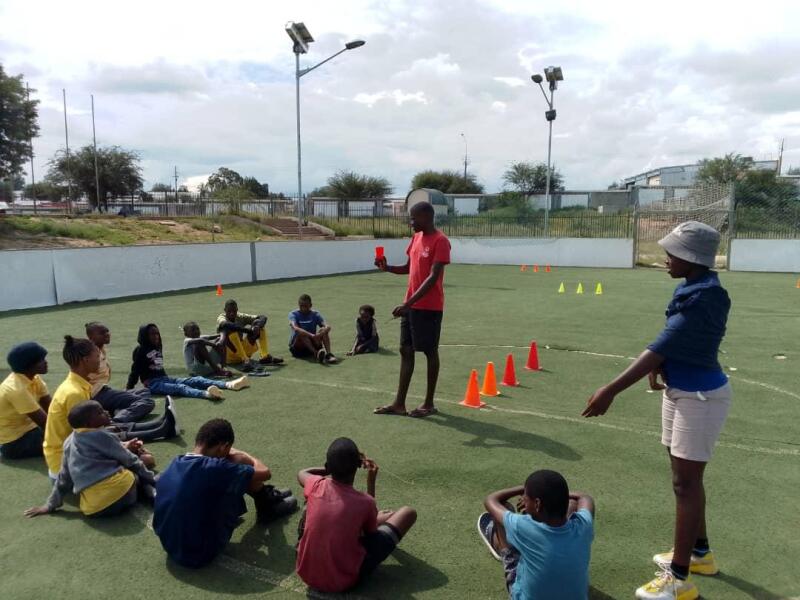 An athlete standing in front of a group of athletes, leading them through a fitness activity outside on a grass field.