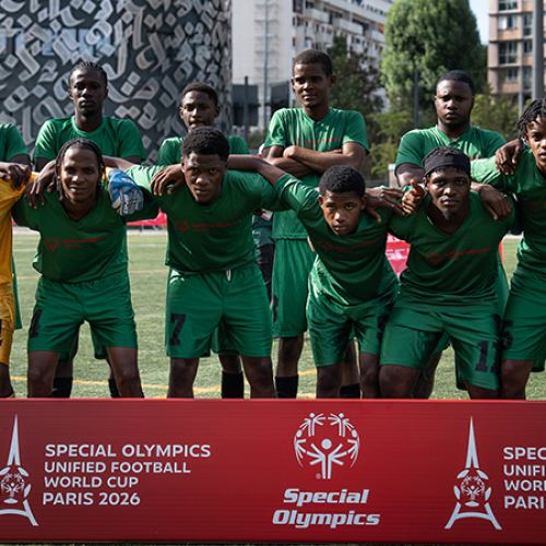 Un equipo de fútbol posa para una foto. Llevan uniformes verdes y están de pie detrás de un cartel rojo que dice "Copa Mundial de Fútbol Unificado de las Olimpiadas Especiales París 2026".