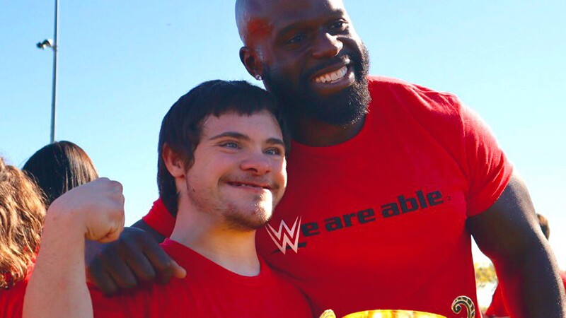 WWE personality and wrestler with his arm around a young athlete holding a golden cup