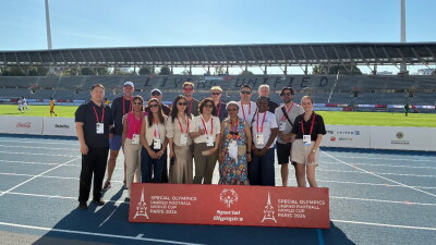 Group of people standing on a track with Unified Football World Cup Paris 2026 signage in front of them with the field in the background. 
