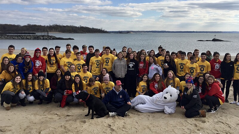 Group of participants, athletes, and representatives on the beach in a group photo.