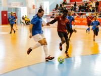 Football match with a player in a blue jersey entering the penalty area to shoot, while a player in a red shirt attempts to block him.