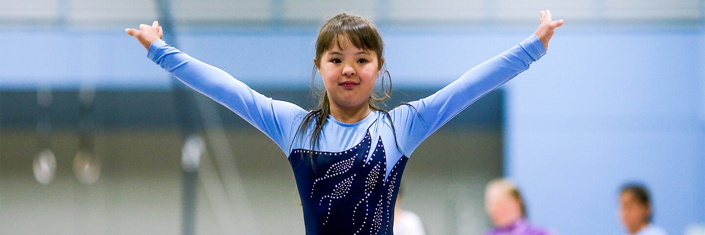 Young girl in a blue leotard raising her arms as she finishes her routine.