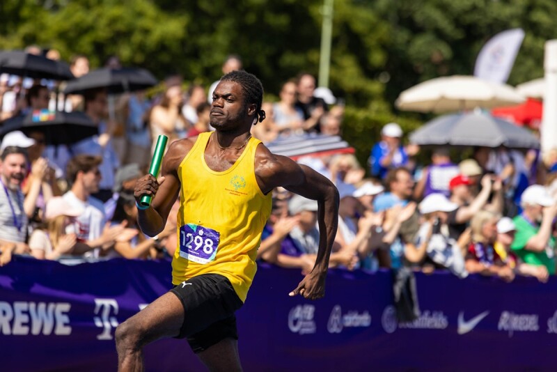 Special Olympics Jamaica sprinter running with a baton in front of a crowd