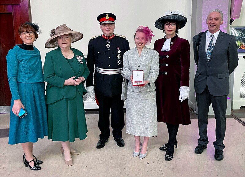 Kiera holding the British Empire Medal, smiling next to the lord-lieutenant, the High Sheriff, and members of Kiera's family.