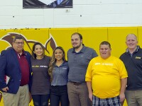 A group of 6 young adults and Rowan and EPSN representatives stand under a Rowan University Unified Champion Schools banner in a gymnasium. 