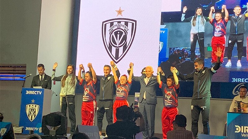 A group of athletes and Special Olympics representatives are on stage holding hands with their arms raised in victory.