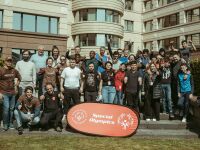 A group of people stand together smiling and with their thumbs in the air in front of a red Special Olympics banner. 