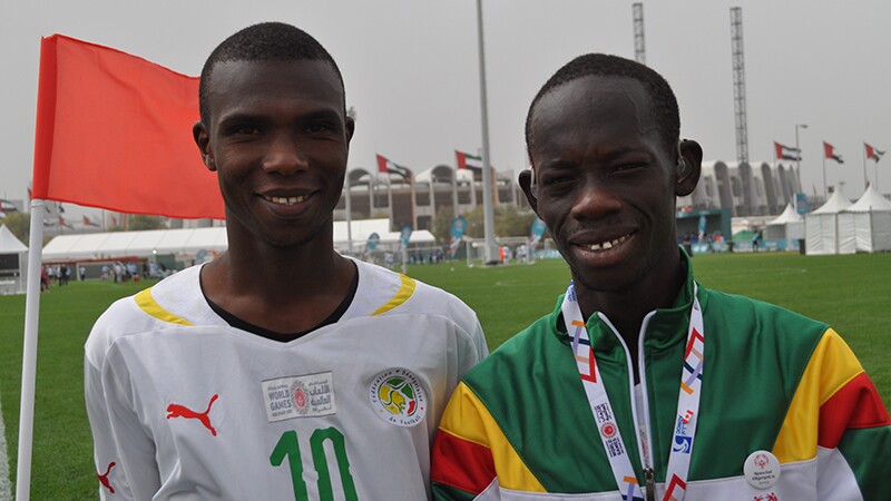 Aboubakrine Sadikh Diaw and Mame Ndiagne Ndiaye standing side by side on the football field. Mame has his hearing aids in.
