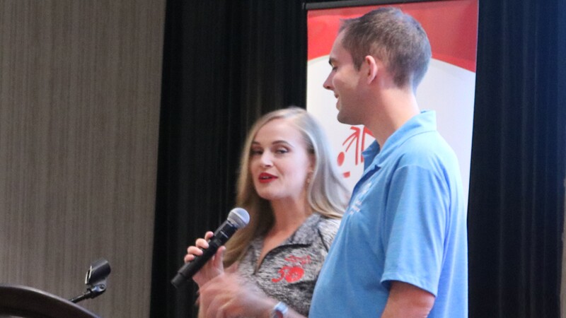 Tyler Leech standing next to a woman speaking into a microphone; both are behind a podium.