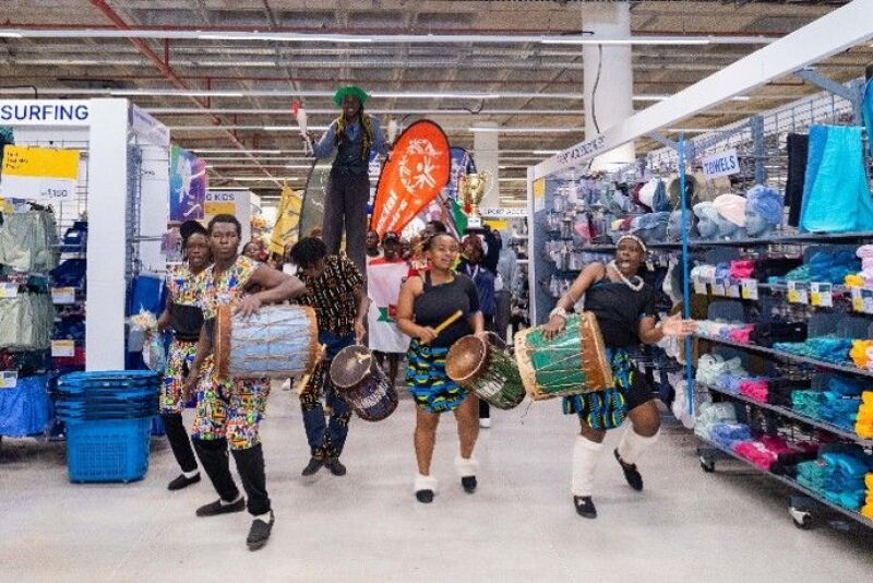 A group of people dance and drum together inside a Decathlon store.