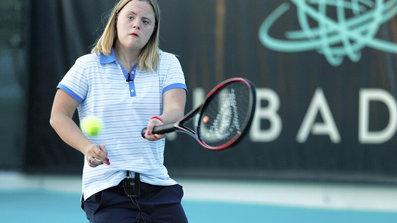 Clara on the court with a tennis racket swinging at the ball.