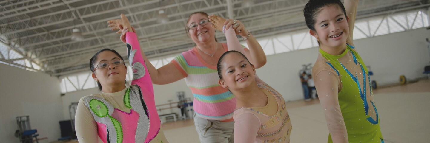 Three athletes pose while a coach assists with hand techniques.
