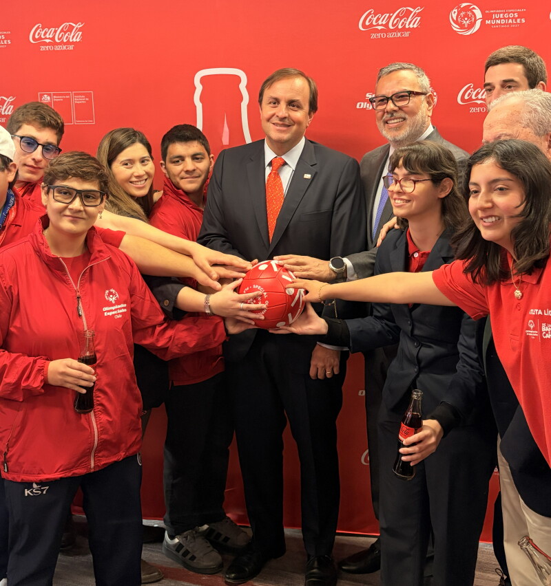 A group of people posing for a photo with their hands on a Special Olympics-branded football at the center.
