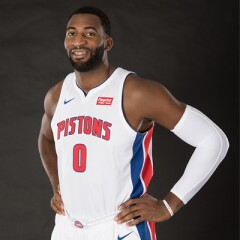 Andre Drummond standing in his pistons uniform with the number 0 on the front, smiling with both hands on his hips