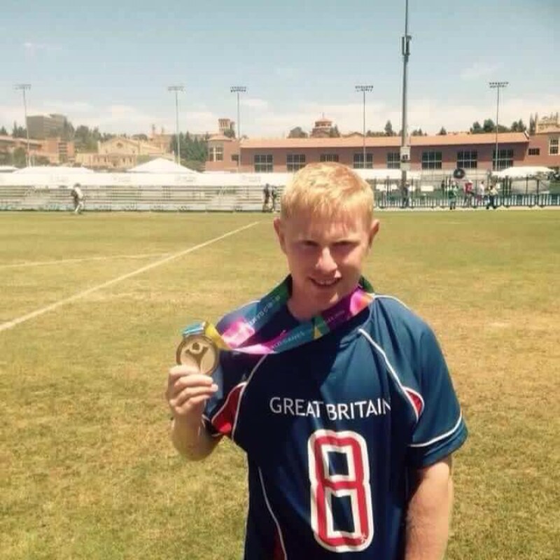 A Special Olympics Great Britain stands on a football field showcasing his gold medal.