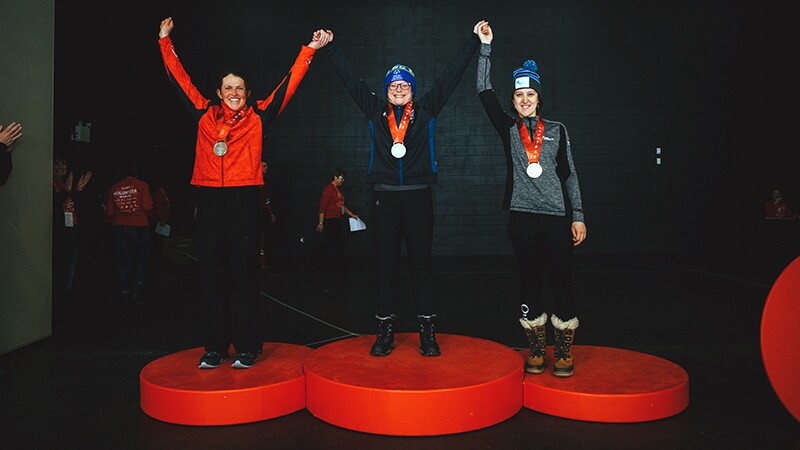 Ashley Adie stands for a picture with two competitors on the podium after receiving a gold medal.