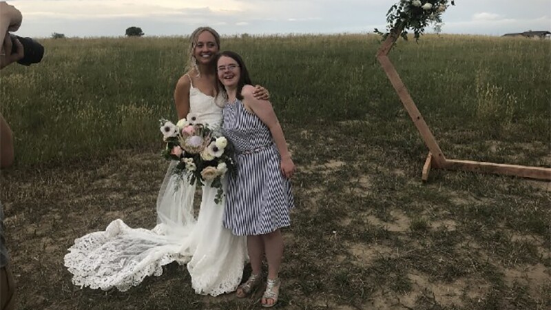 Hanna standing next to a bride as the bride holds a bouquet and has her arm around Hanna's shoulder.