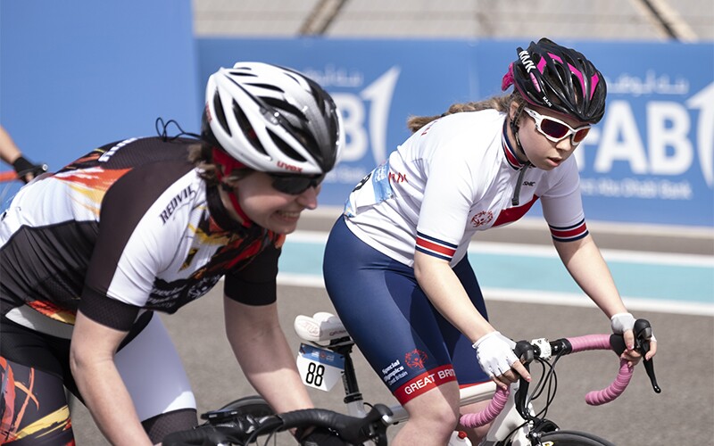 Kiera riding her bike next to another athlete. Both have safety helmets on.