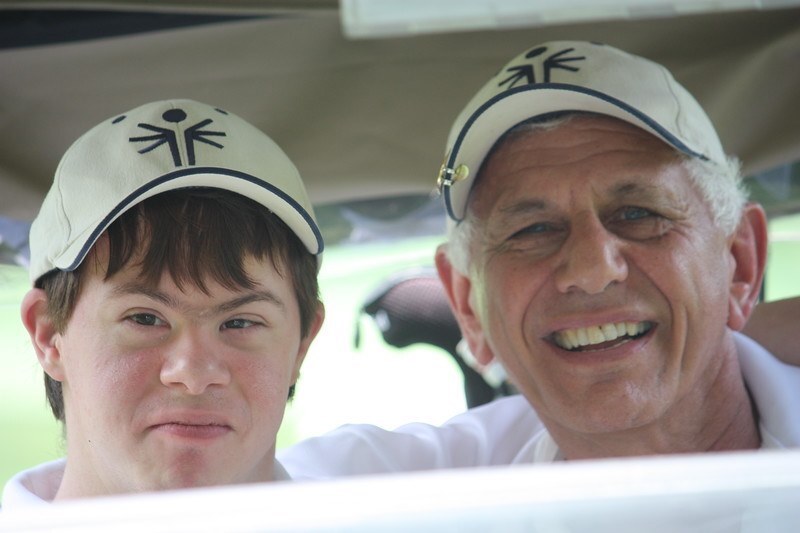 A Special Olympics athlete and coach sit in a golf cart and smile at the camera. 