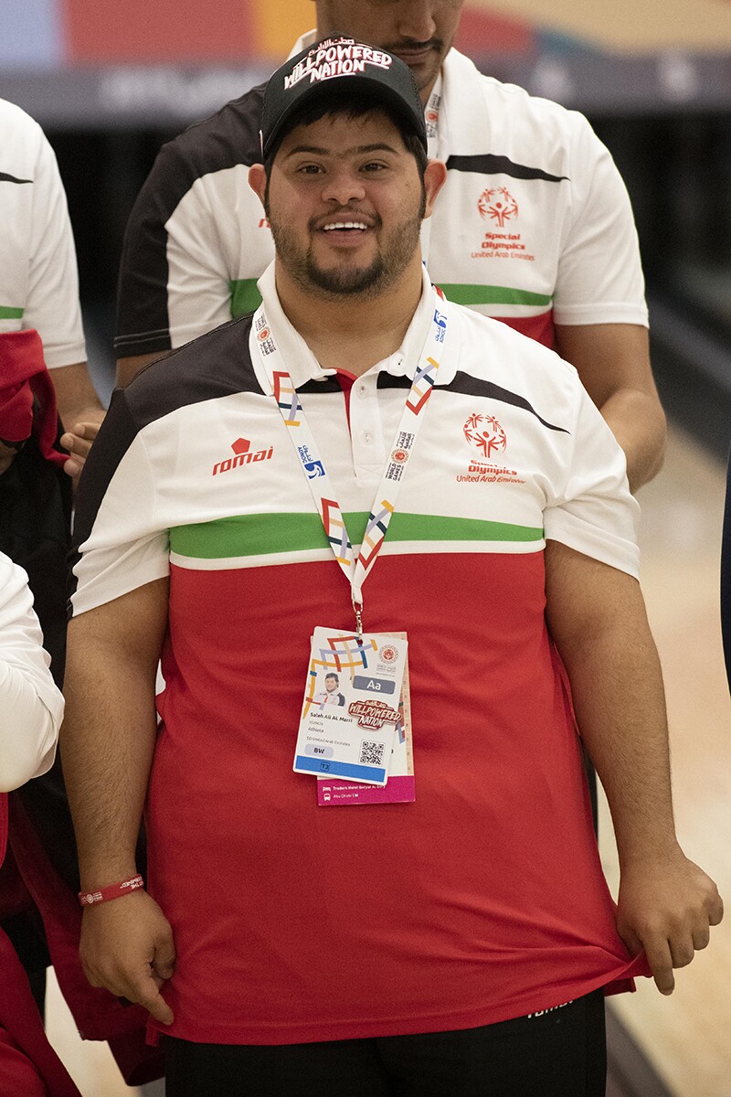 Saleh Al Marri standing for this photo. He has on a red white and green Special Olympics United Arab Emirates polo.