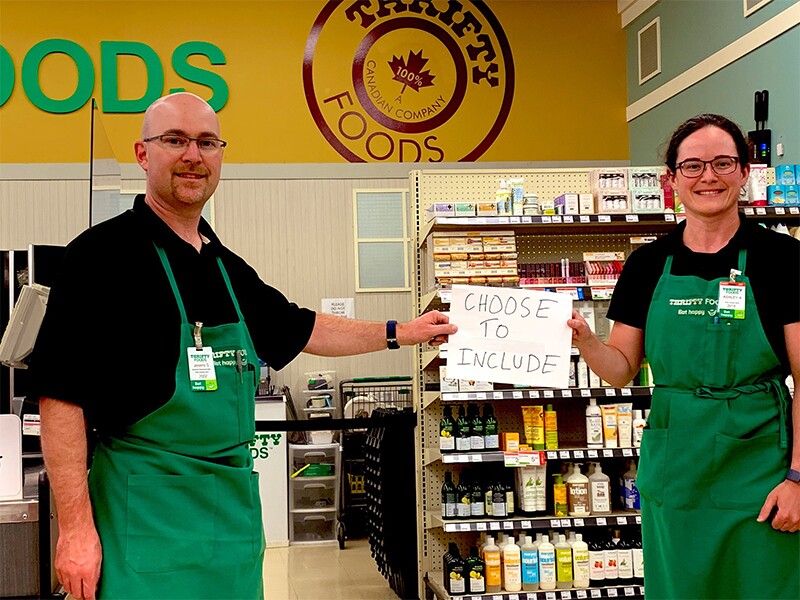 Ashley stands with a coworker, both holding a sign that reads ‘Choose to Include.'