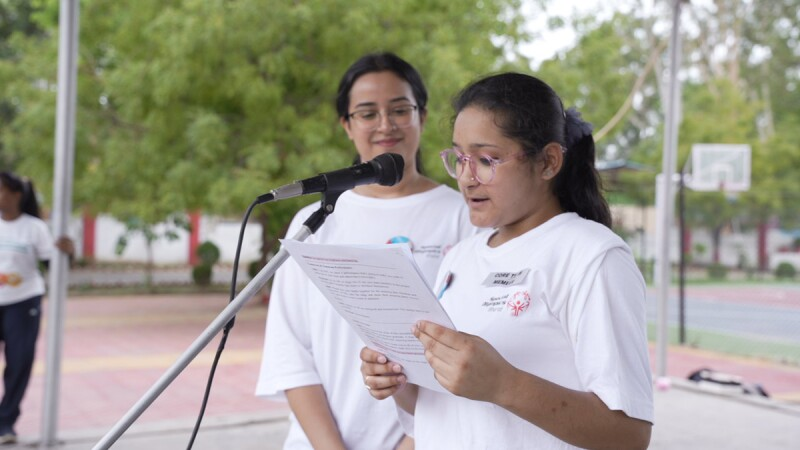 A lady stood in front of a microphone reads from a sheet of paper she's holding