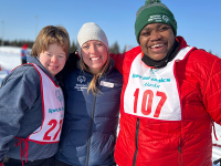A group of three people pose for a photo. They are outside wearing heavy winter coats and the ground is covered in snow. 