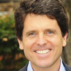 Mark Shriver smiling for a professional photo. He's outside in front of greenery.