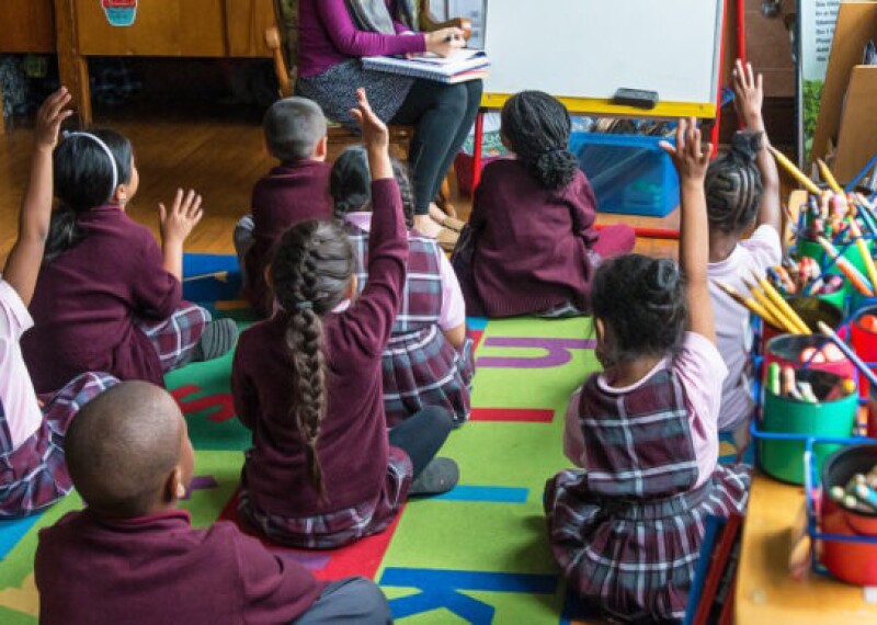 Kids in a class room raising their hands.