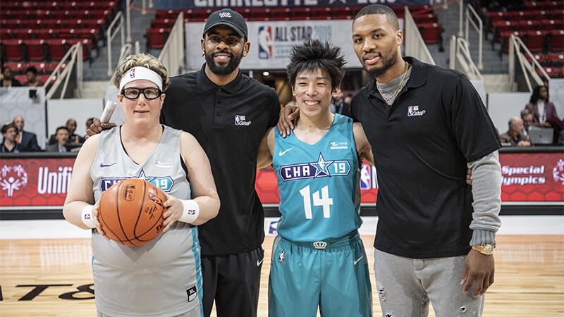Two NBA players standing behind two Special Olympics athletes on the court.