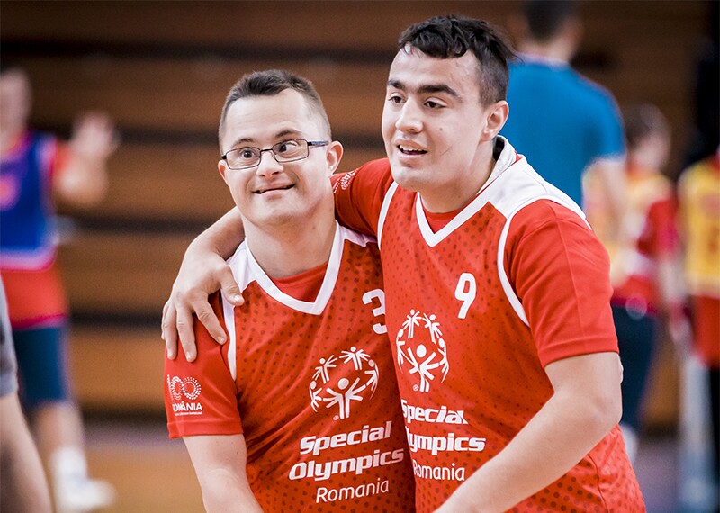 Two athletes from Special Olympics Romania on the court with their arms around one another's shoulders showing camaraderie.