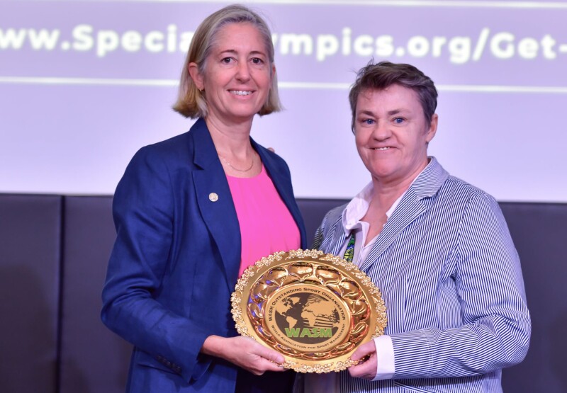 Dos mujeres están una al lado de la otra mientras sostienen un premio y sonríen para una foto. 