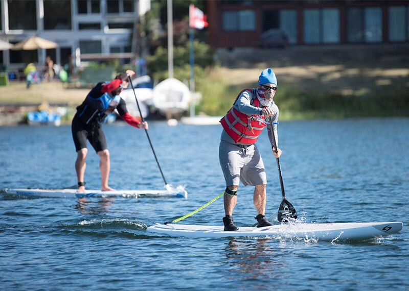 Two athletes standing up and paddling on long board in the water.