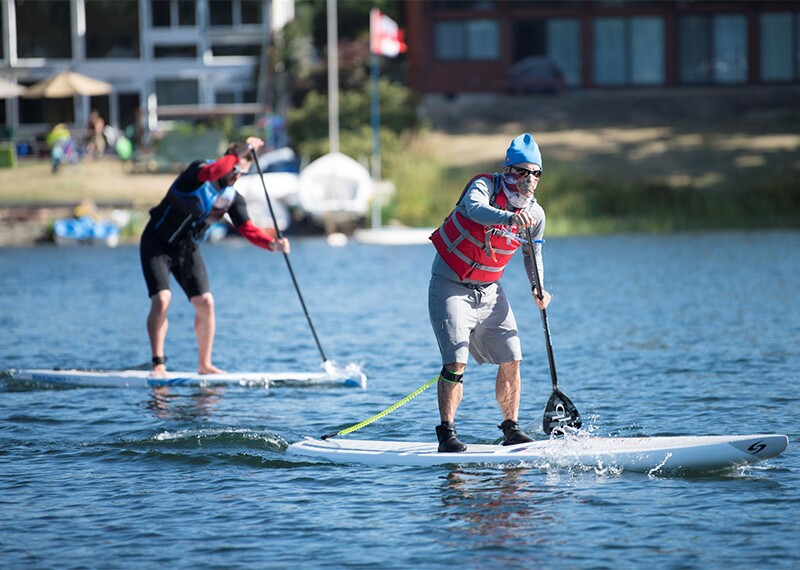 Two athletes standing up and paddling on long board in the water. 