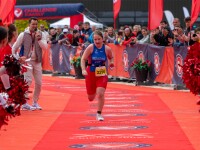 A woman in red and blue athletic kit runs towards the finish line with cheerleaders surrounding her. 