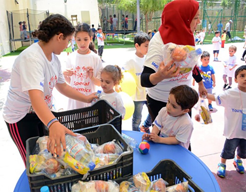 A candid photo of two adults handing out snacks to children. 