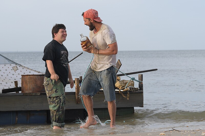 Zack Gottsagen and Shia LaBeouf laugh in front of a raft while filming The Peanut Butter Falcon.