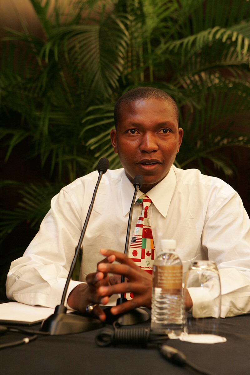 Ephraim Mohlakane sitting at a table speaking with a microphone in front of him.