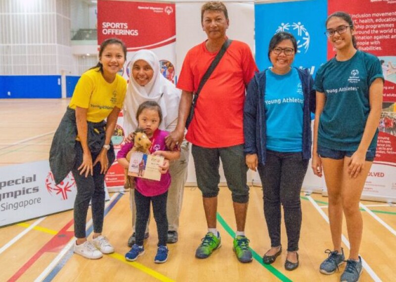 Hadbaa at a young age stands in front of Special Olympics Singapore signs with her family.