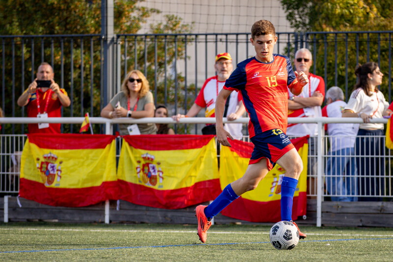 Footballer on the pitch dribbling the ball across the field, spectators are in the background. 