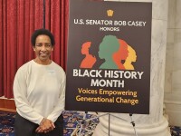 Loretta stands next to a sign that reads, “U.S. Senator Bob Casey Honors Black History Month. Voices Empowering Generational Change.”