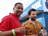 A Special Olympics athlete in a red shirt smiles for the camera. He's standing next to a man outside. 