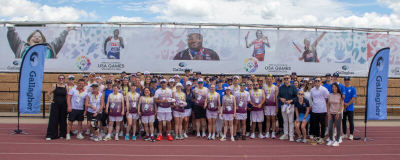 A large group photo of people standing on a racetrack in front of Special Olympics branded banners. 