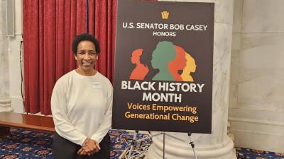 Loretta stands next to a sign that reads, “U.S. Senator Bob Casey Honors Black History Month. Voices Empowering Generational Change.”