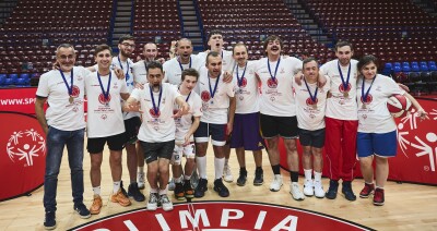 A group large of basketball players stand together smiling on court.