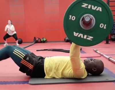 Banele laying on the ground in a gym doing chest presses. 