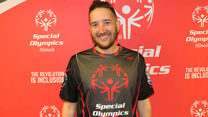A man stands in front of a red background and smiles for a photo.