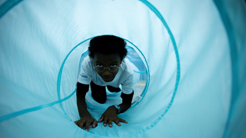 Young athlete crawling through a blue material tube